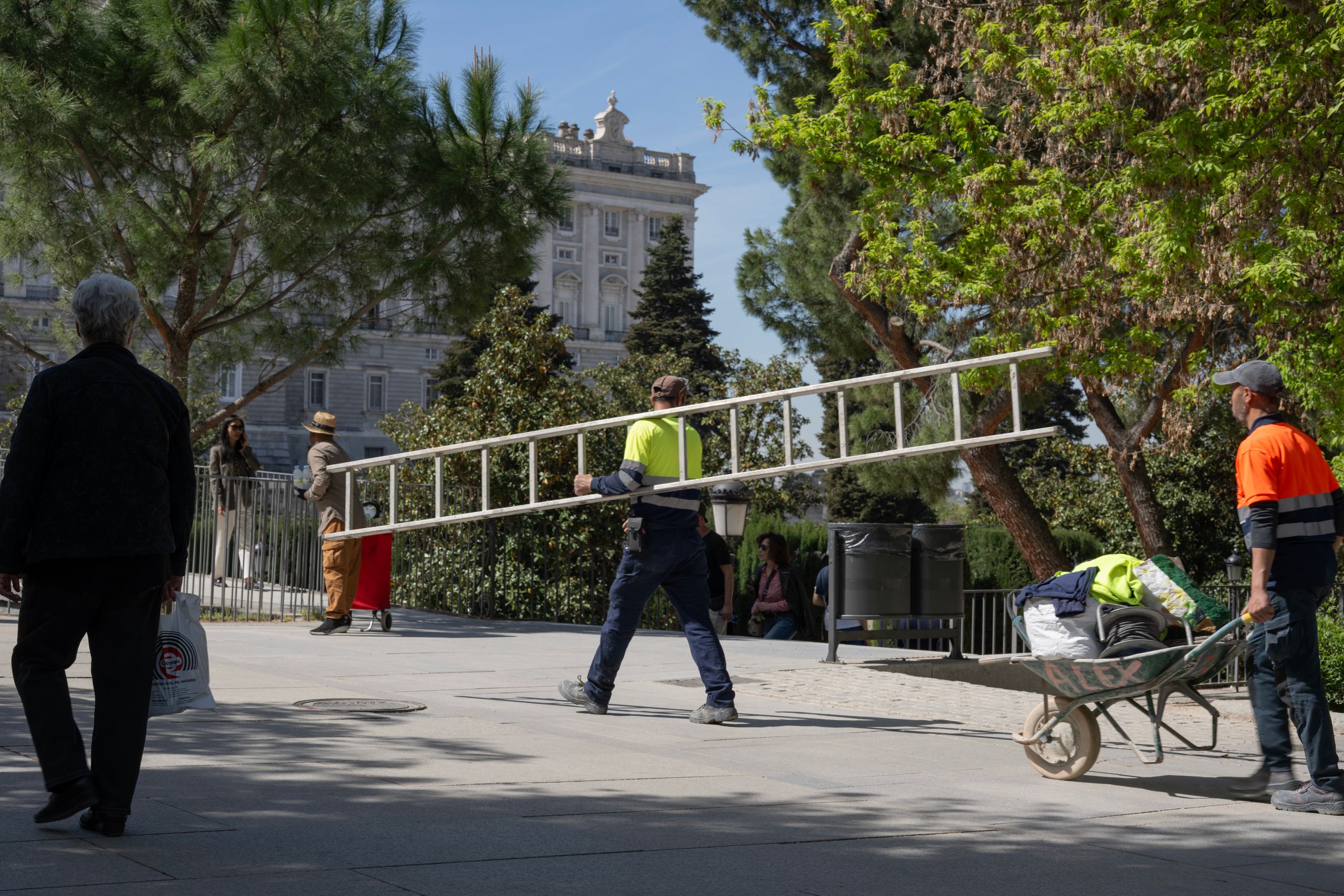 Workers carrying a ladder on a sunny day in Madrid near a historic building.