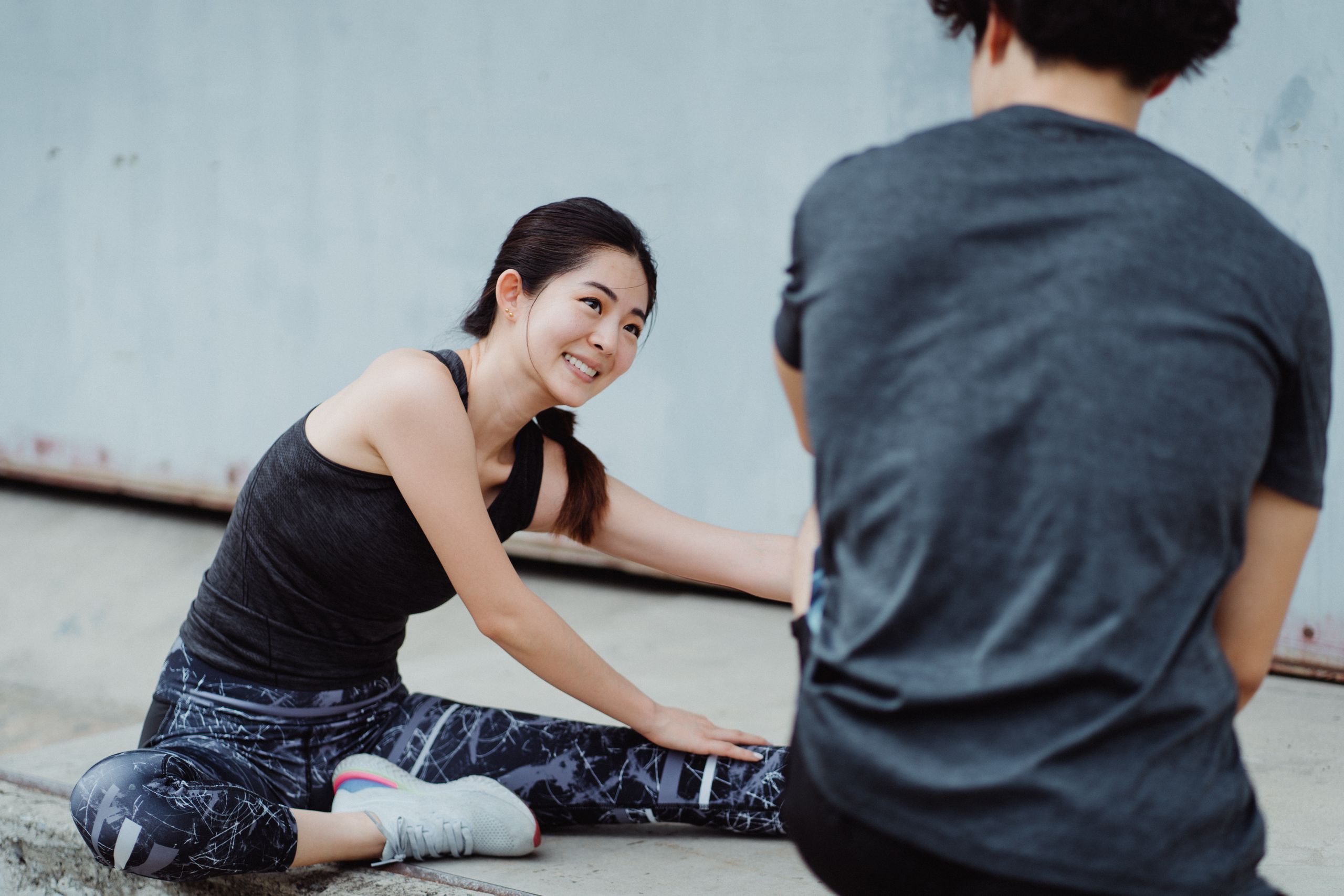Young Asian woman smiling while stretching outdoors during a fitness session.
