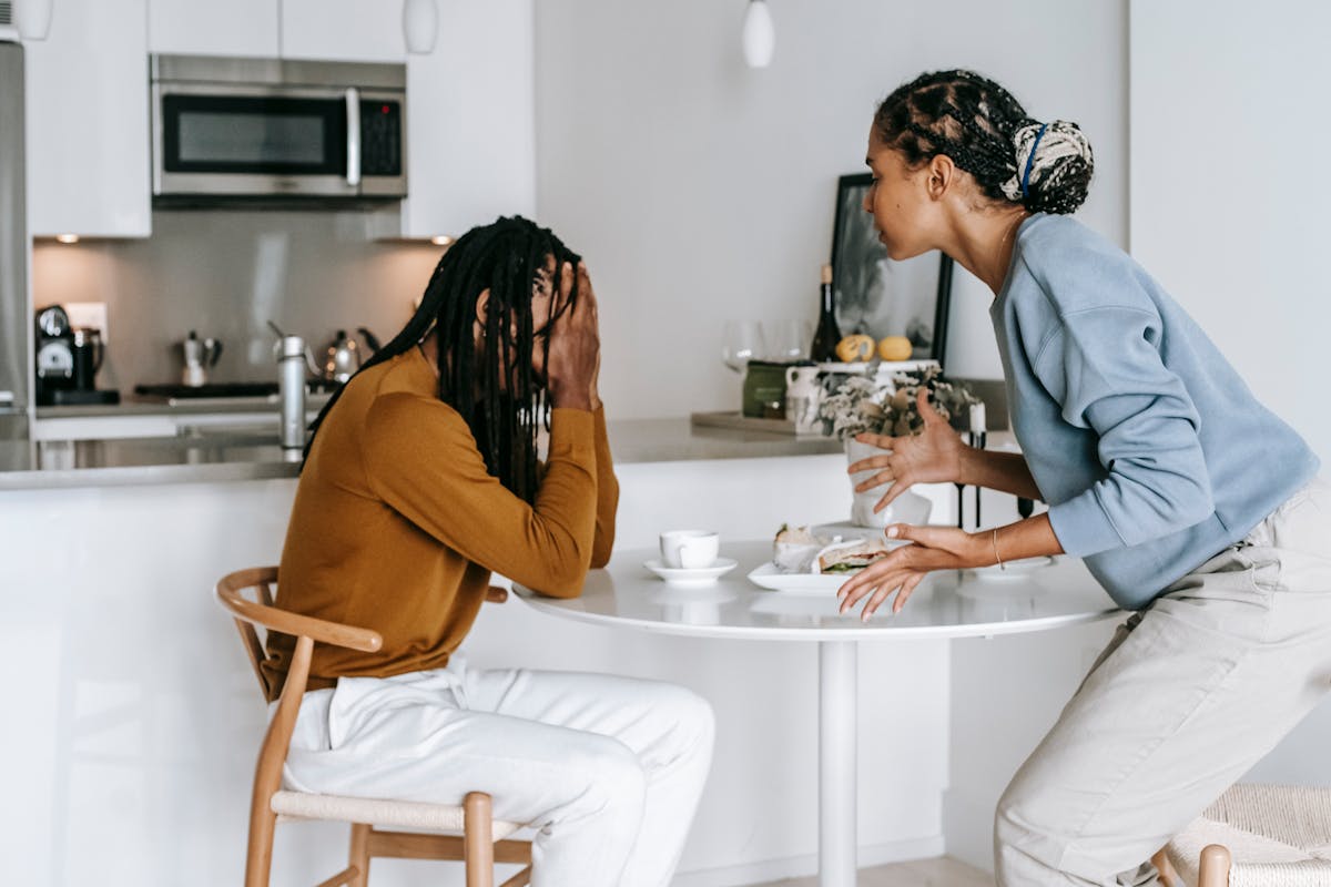 10 Obvious Signs Someone Is Completely Losing Themselves 2 Young black man sitting at table with hands on head and having conflict with standing near table woman in light kitchen