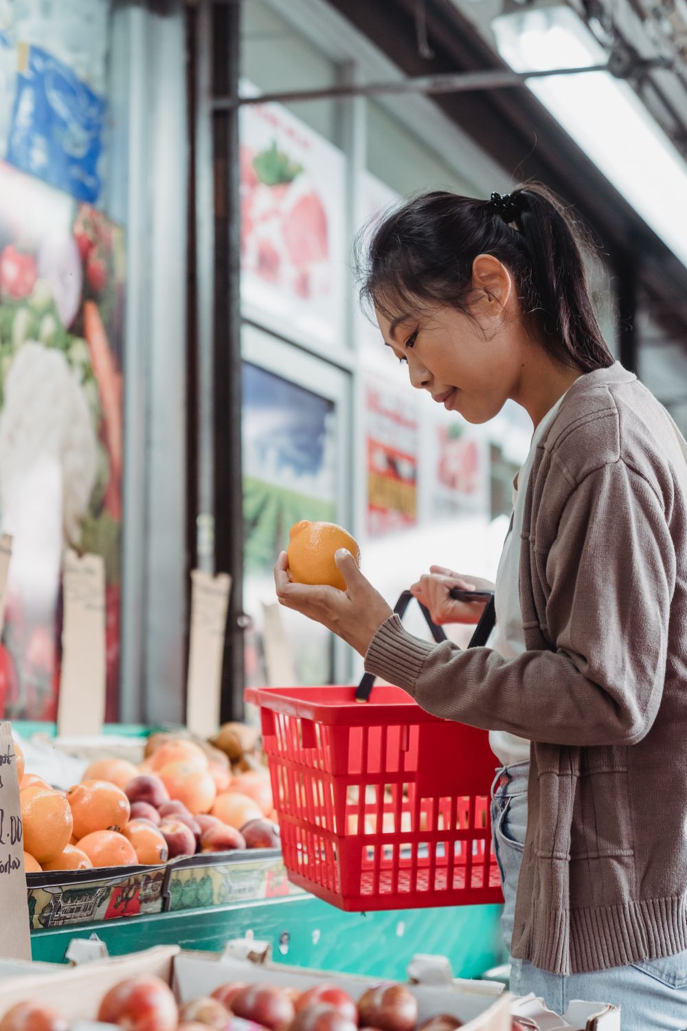 Young woman in a market selecting a fresh apple from a basket of fruits, indoors.