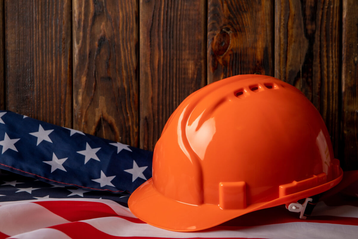 American flag and safety helmet on wooden background, space for text