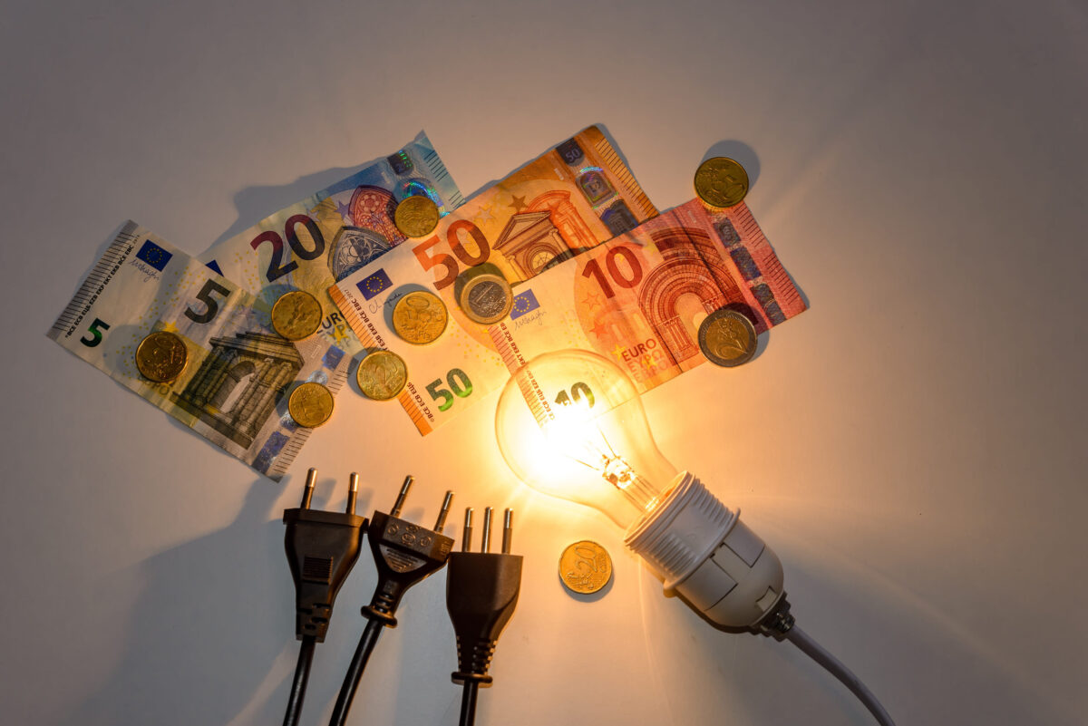 Light bulb lit with bills, coins, banknotes and electric plugs. Increase in energy tariffs and prices.