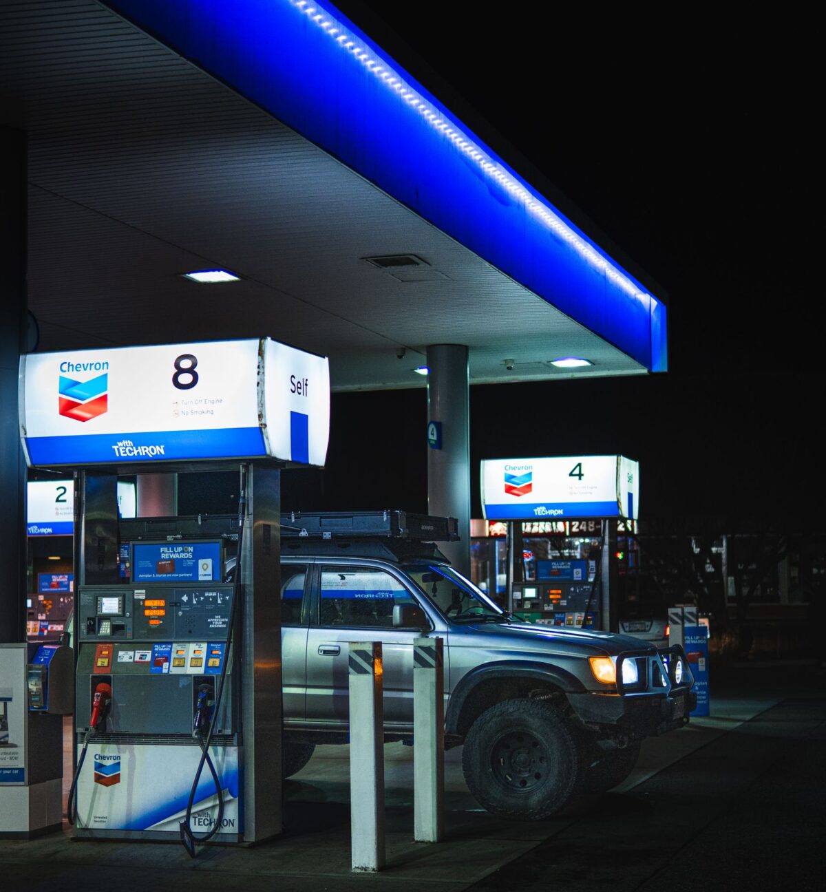A 4x4 parked at a Chevron gas station at night, highlighting fuel pumps and station lights.