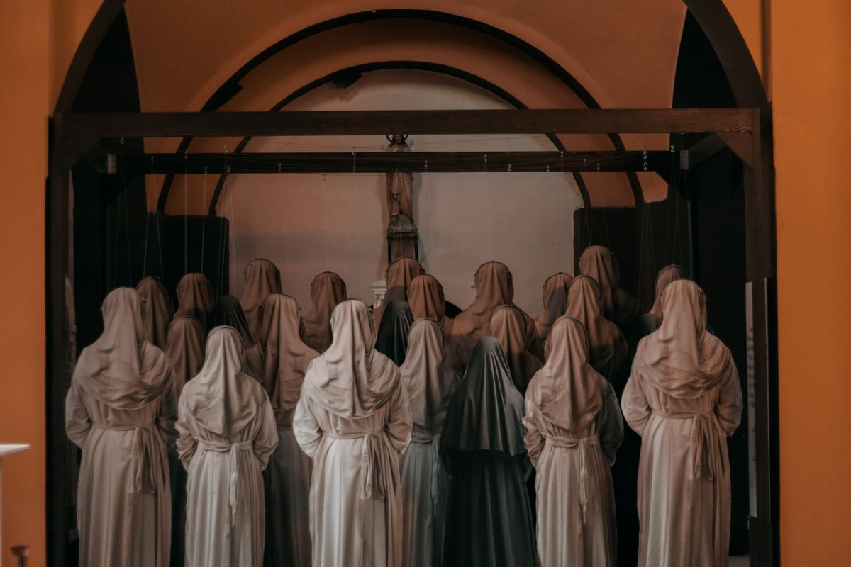 A group of nuns dressed in habits standing in prayer at a chapel altar.
