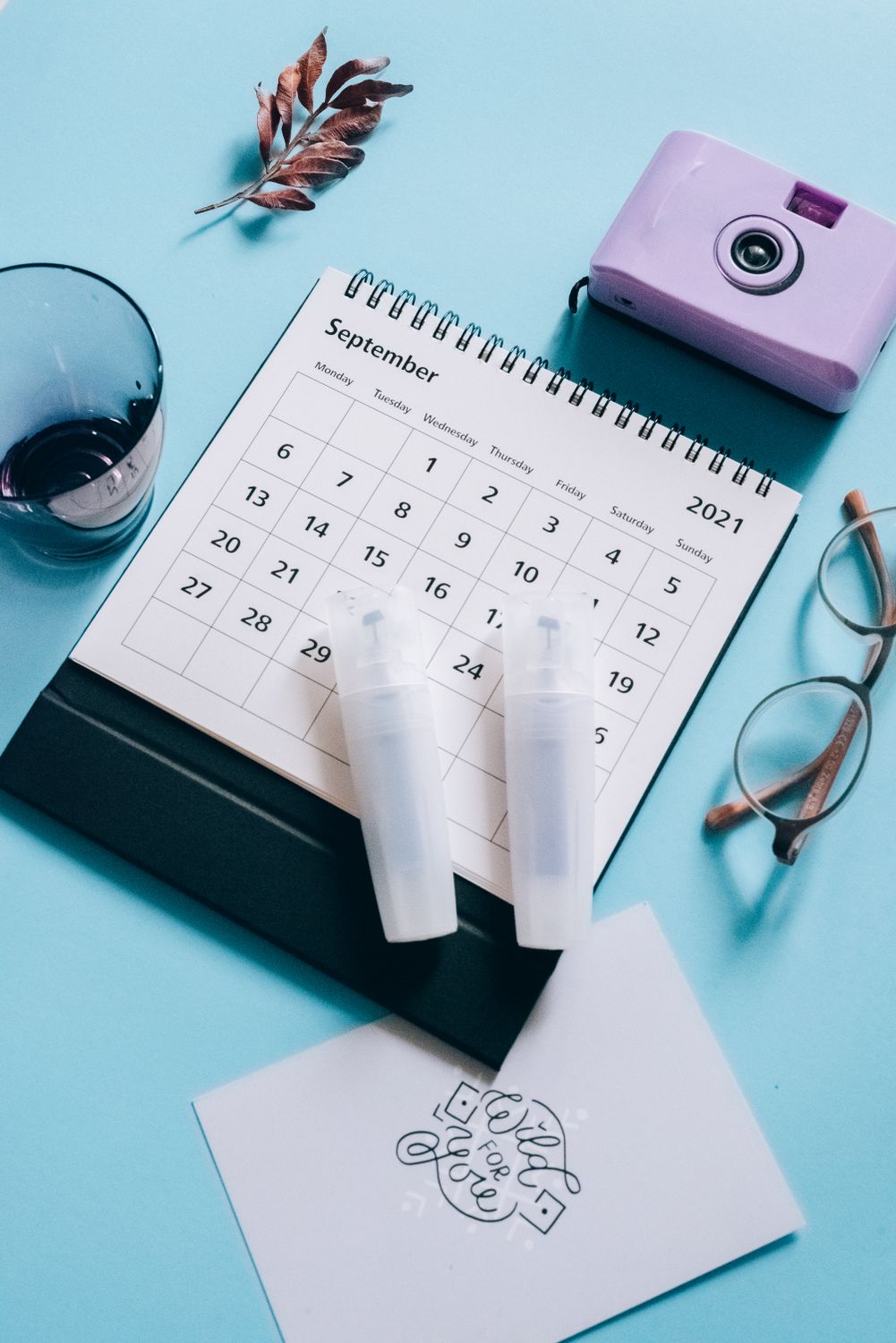 A minimalist arrangement of calendar, camera, and glasses on a blue surface.