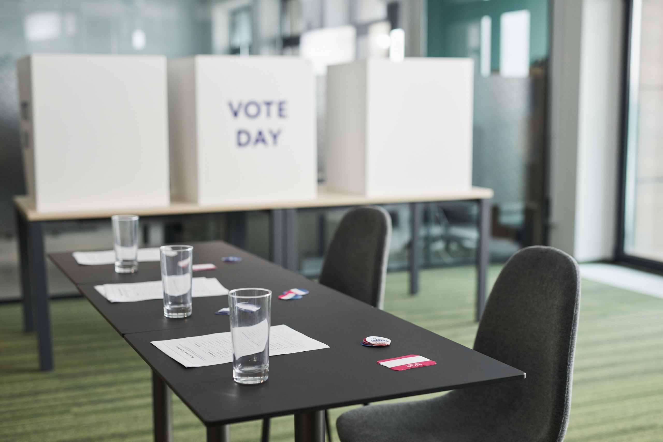 A prepared voting station with tables, chairs, and privacy booths in a conference room.