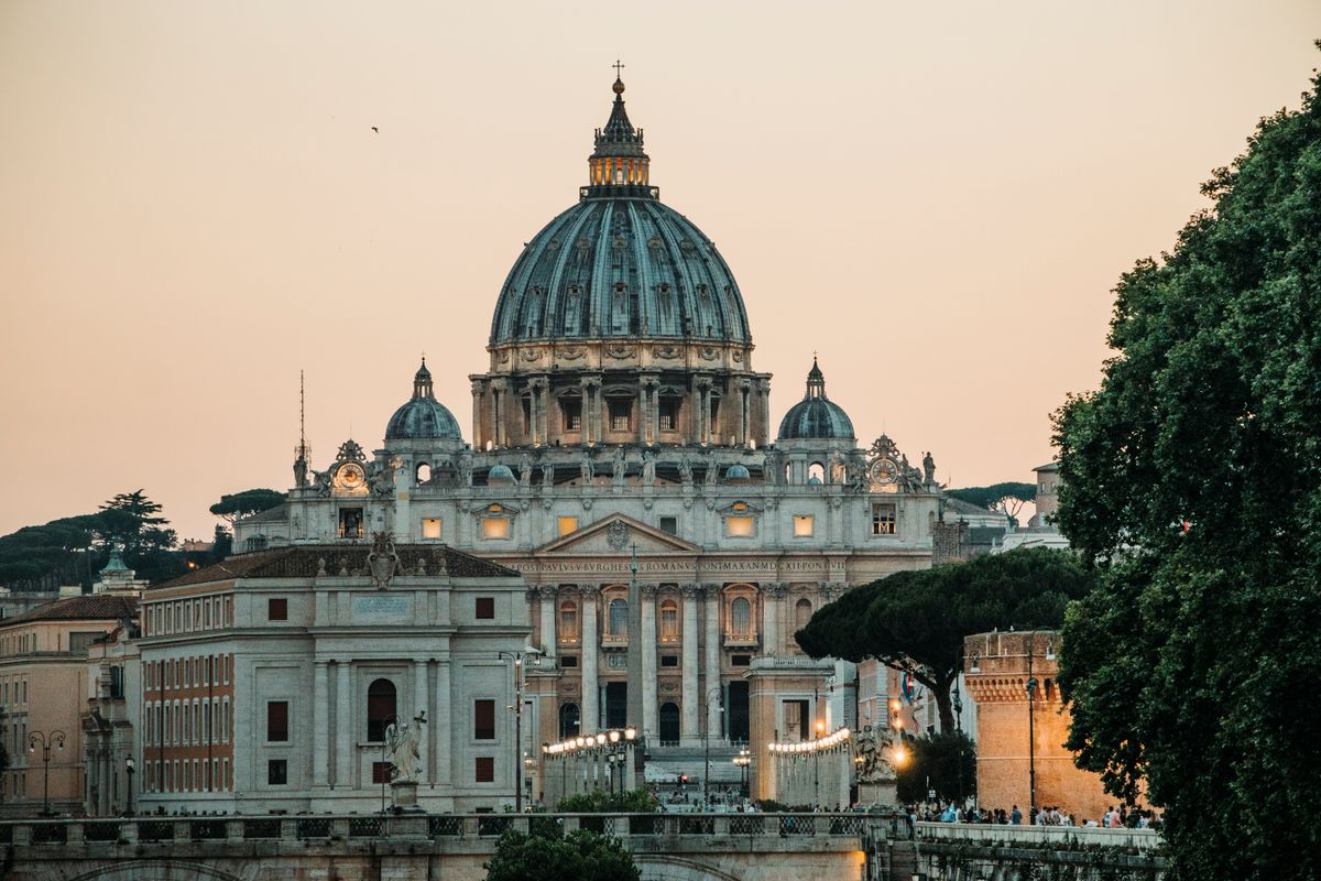 A stunning view of St. Peter's Basilica with a warm sunset backdrop in Vatican City.