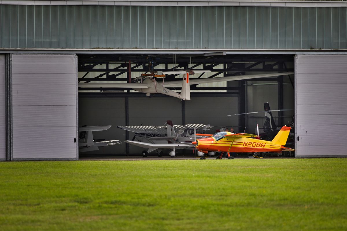 The Fighter Jet Race Is Changing as New Technology Redefines the Future of War 4 A vibrant yellow plane parked outside a hangar full of aircrafts on a sunny day.