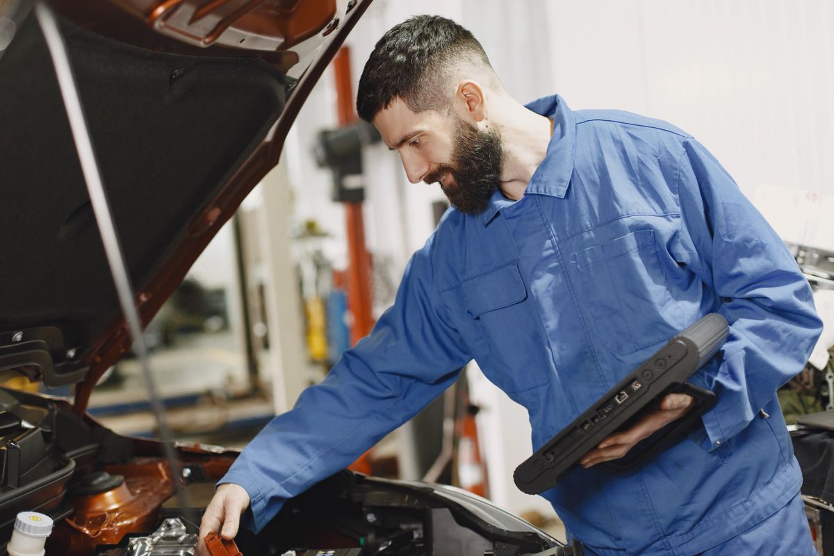 Trump’s Right to Repair Push Could Cut Car Repair Costs for Drivers 1 An auto mechanic in blue coveralls inspecting a car's engine in a garage.