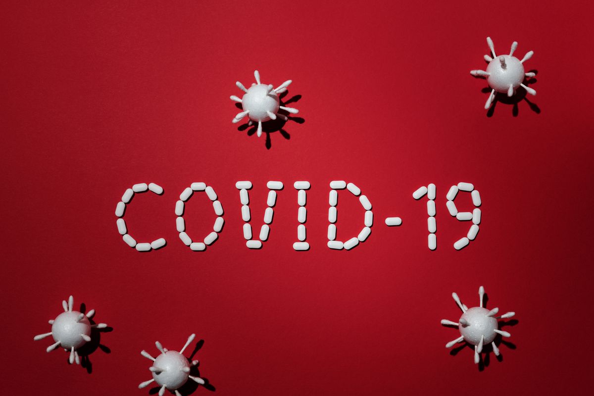 Artistic representation of COVID-19 using pills and virus models on red background.