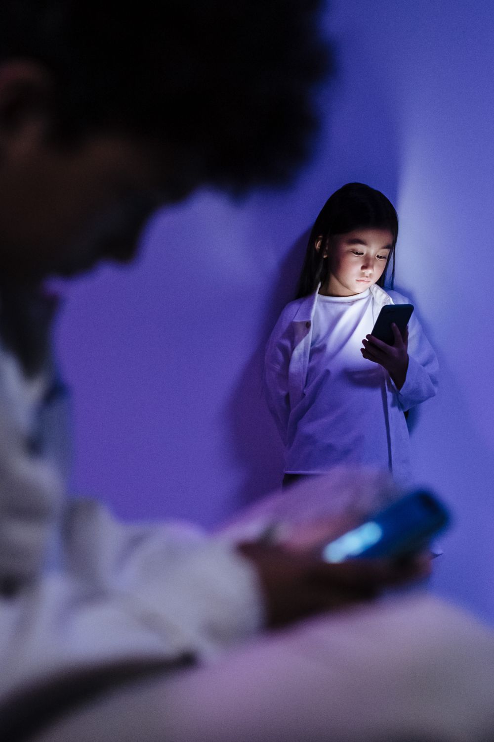 Children absorbed in smartphone screens under soft blue light, creating a contemplative mood.