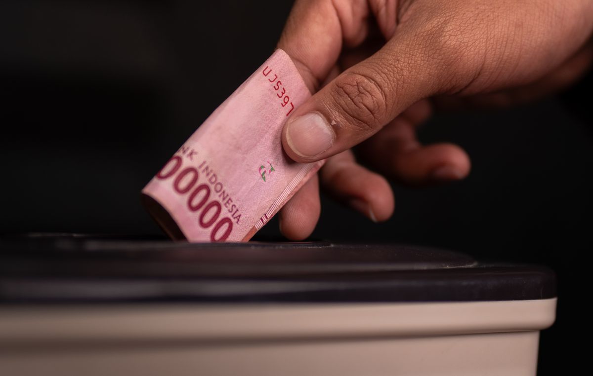 DNC Puts Headquarters on the Line for $15 Million Loan as Debt Overtakes Cash 2 Close-up of a hand donating an Indonesian Rupiah note into a charity box, symbolizing generosity.
