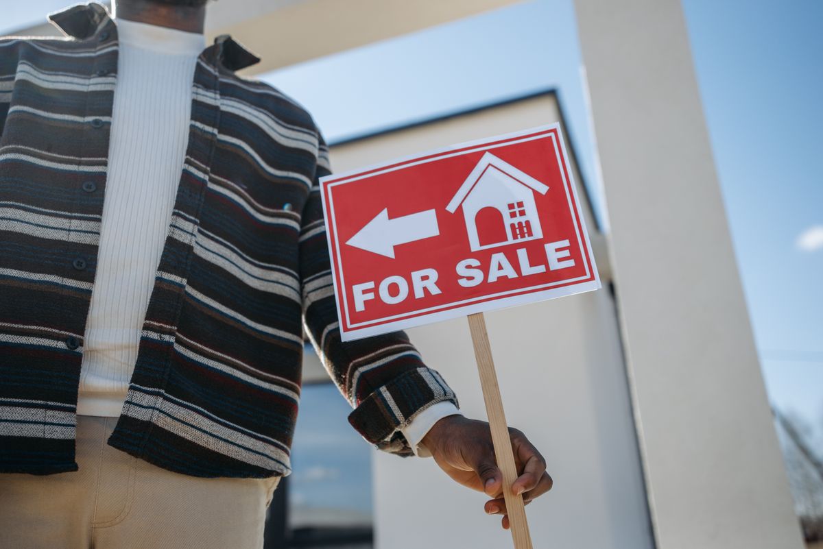 America’s Housing Market Is Facing a New Problem: Too Few Buyers, Not Just Too Few Homes 3 Close-up of a person holding a for sale sign outside a modern house.