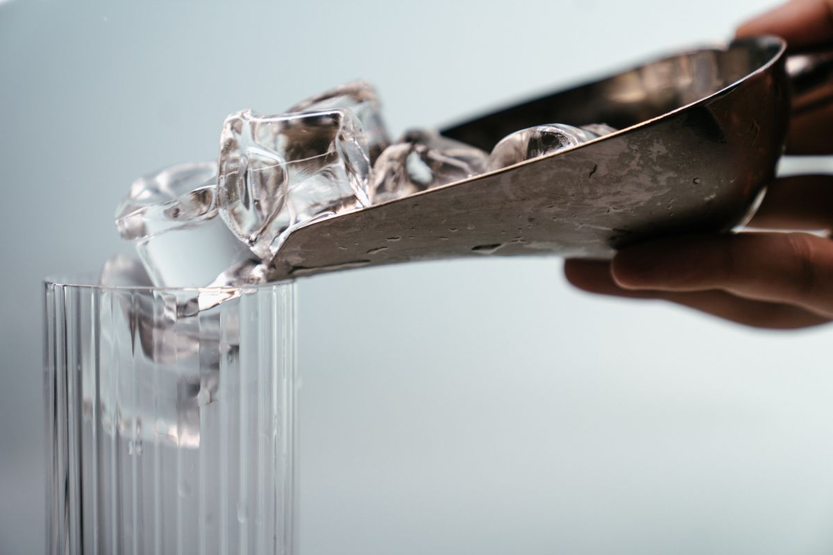 Close-up of metal scoop pouring ice cubes into a highball glass. Perfect for drink concepts.