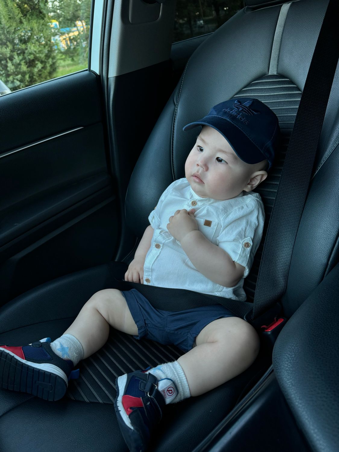 Florida Daycare Community Reels After Toddler Is Found Dead Inside Father’s SUV 1 Cute toddler wearing a cap and shoes, seated safely in a car seat, looking curious.