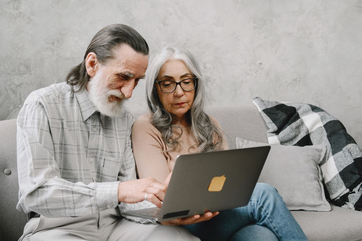 Elderly couple sitting on a couch using a laptop, sharing a moment of togetherness.