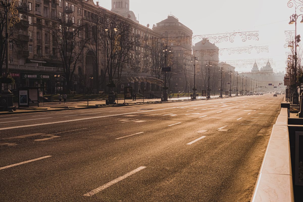 Empty asphalt roadway going through city street with old buildings and lampposts with leafless trees