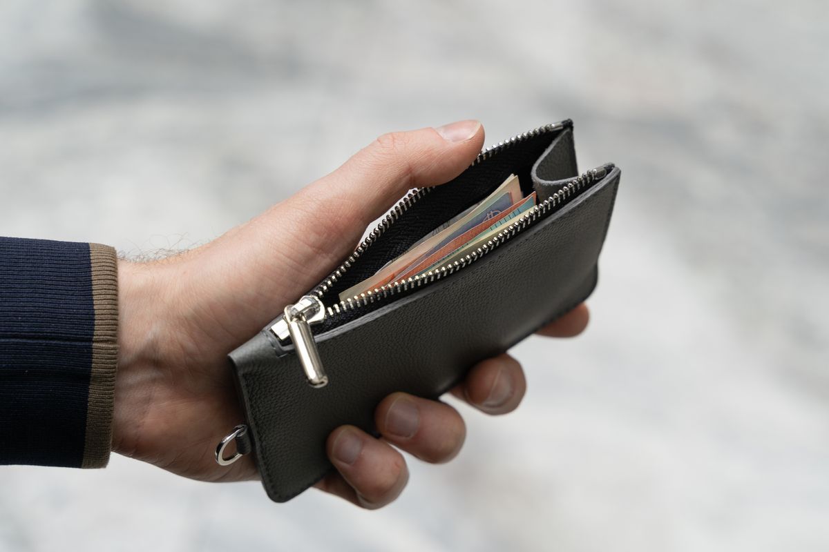 Thrift-Shop Wallet Hides A Chilling Surprise: Bag Marked ‘Uncle Joe Disney’ Leaves Buyer Searching For Answers 1 Hand holding a leather wallet with visible cash, emphasizing finance and savings.