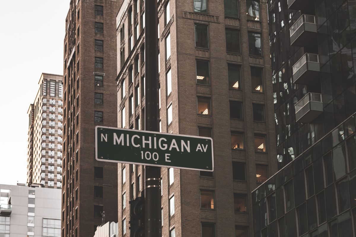 These U.S. Places Are Paying Americans Thousands to Move in 2026: Up to $55,000, $12,000 Cash Bonuses and More. 1 Low angle view of Michigan Avenue sign amidst towering Chicago skyscrapers.