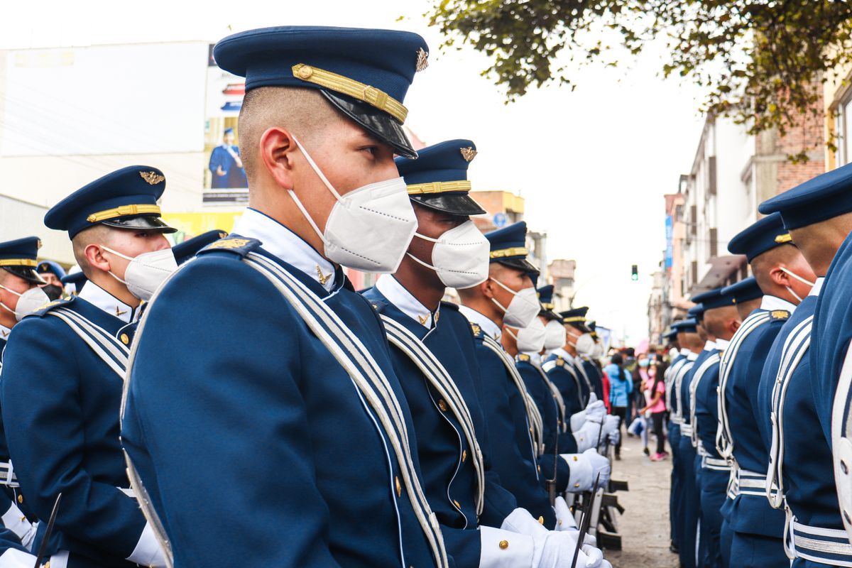 Soldiers in ceremonial uniforms wearing face masks marching in a parade on a street in Ecuador.