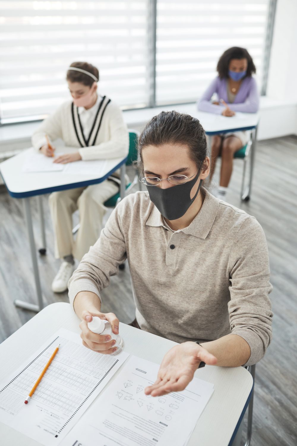 Students wearing masks sanitize hands while socially distancing in a classroom setting.