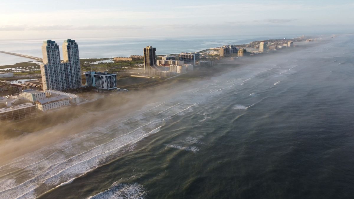 Stunning aerial shot of South Padre Island's coastline with misty waves and urban skyline.