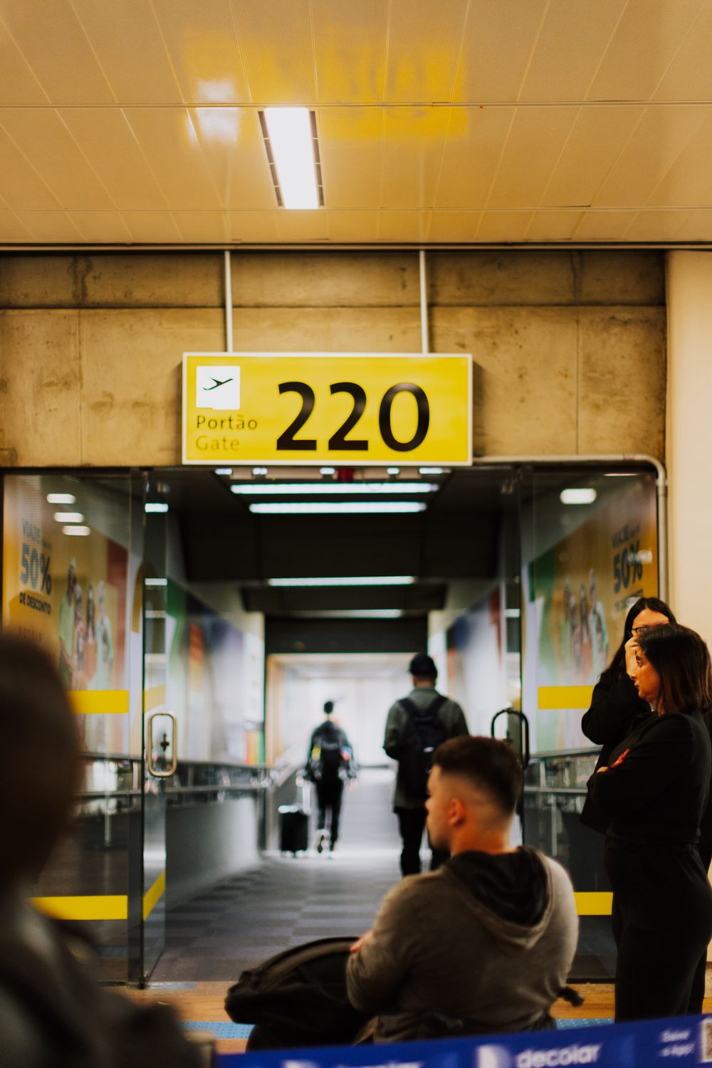 ICE Airport Arrests Expand as TSA Data Sharing Targets Visa Overstays and Travelers With Pending Cases 3 Travelers waiting at a bustling airport gate with a focus on the entrance and sign.