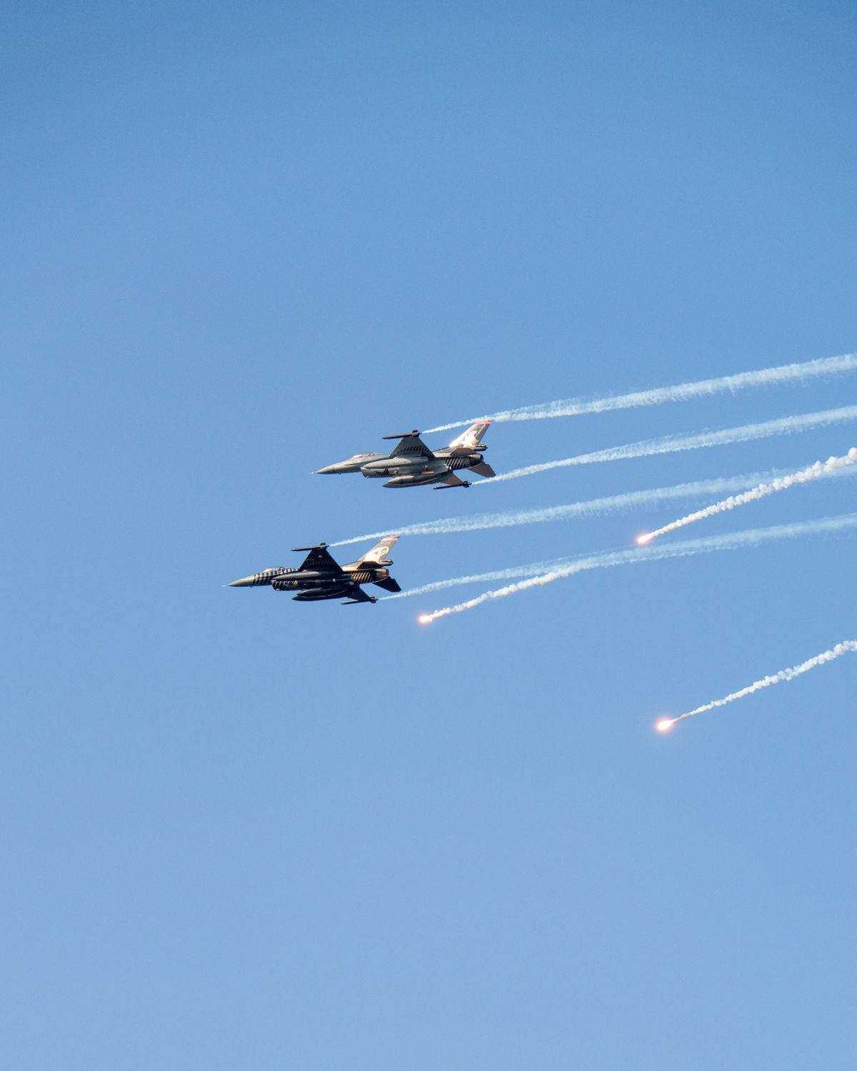 Two military fighter jets perform aerobatic maneuvers against a clear blue sky.