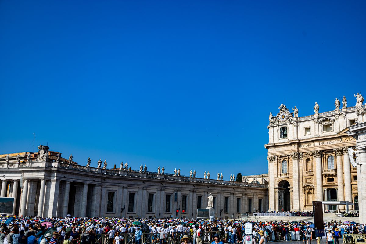 Vibrant crowd at St. Peter's Basilica in Vatican City under a clear blue sky.