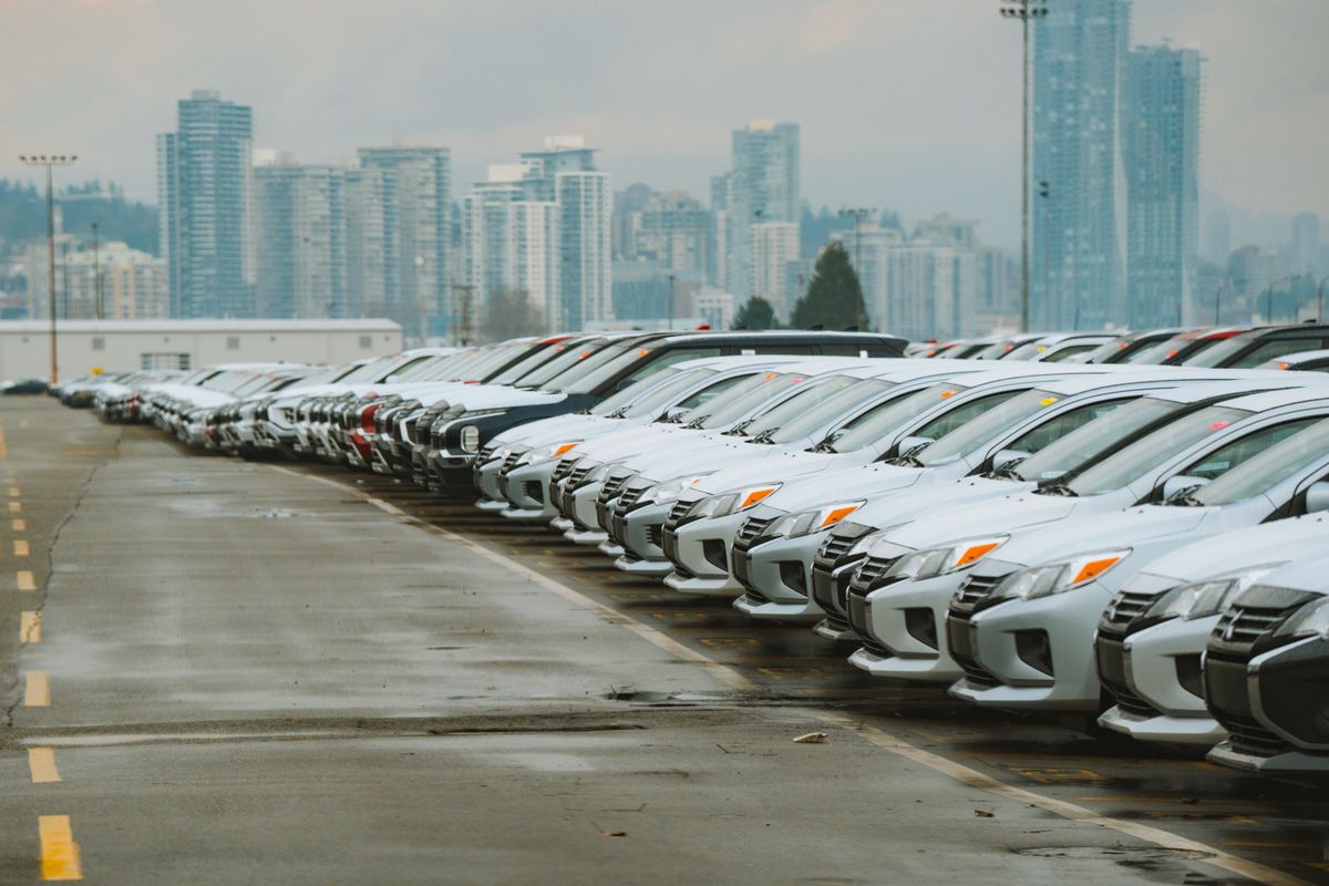 Trump’s Tariff Defense in Michigan Sparks New Fight Over America’s Auto Future: Jobs, Prices and the High Stakes Behind ‘America First’ 1 White cars lined up in a parking lot with a city skyline backdrop.