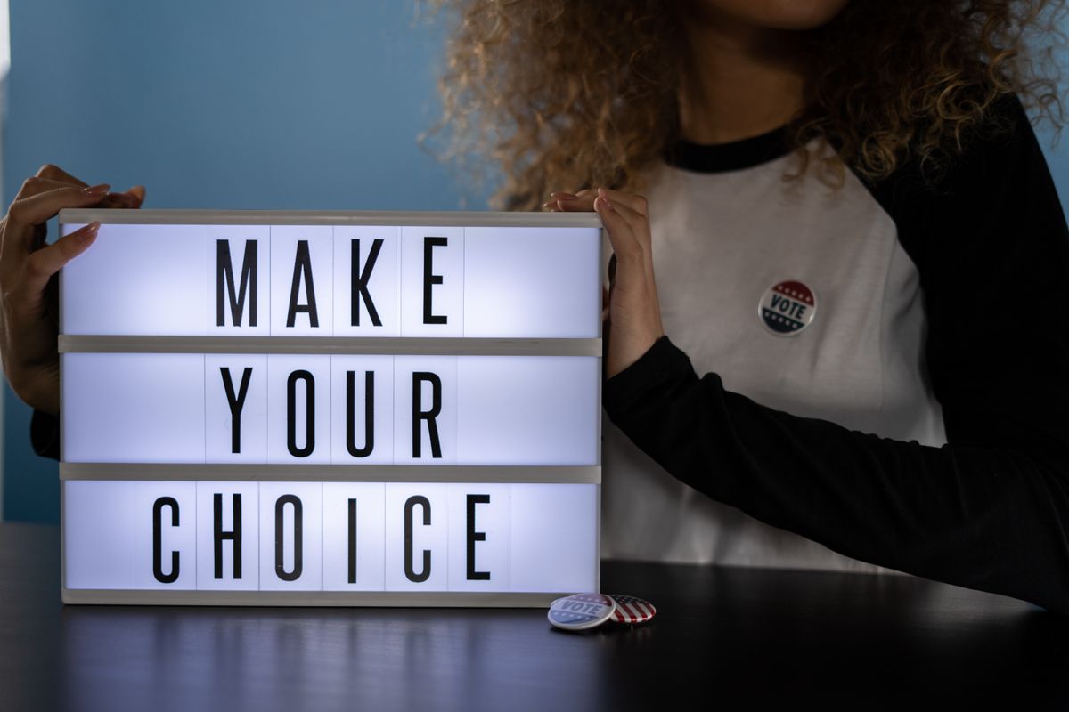 A woman is holding a lightbox with 'Make Your Choice' promoting civic duty and voting.