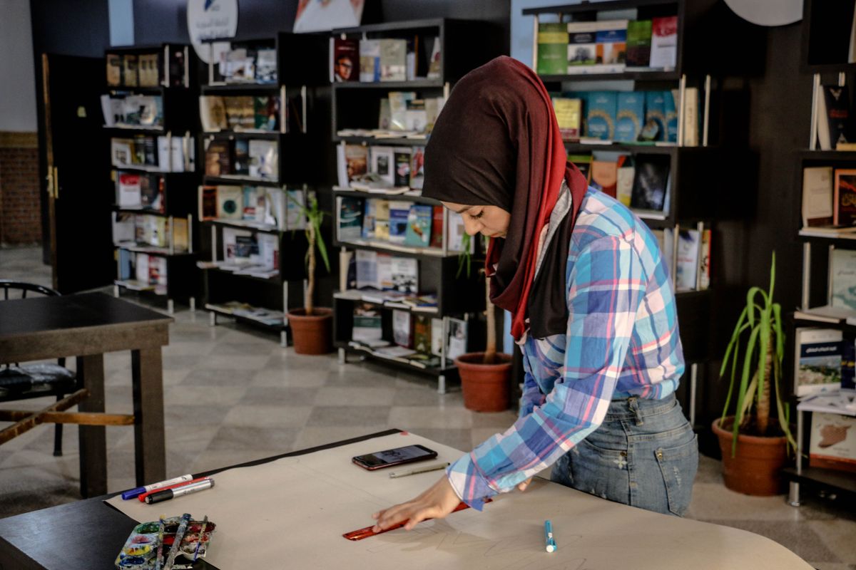 Woman in a library creating art on a large paper with books around her.