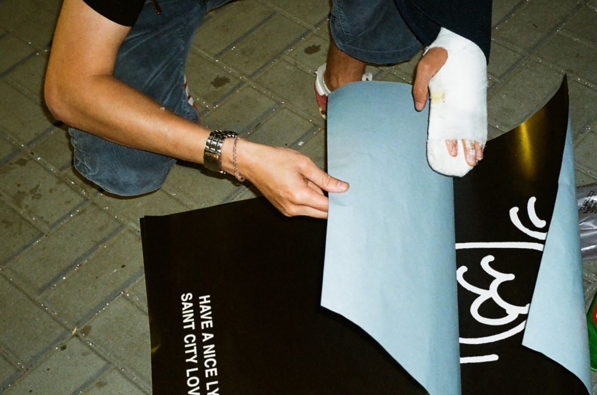A close-up of a person handling street posters with a bandaged hand on a city sidewalk.