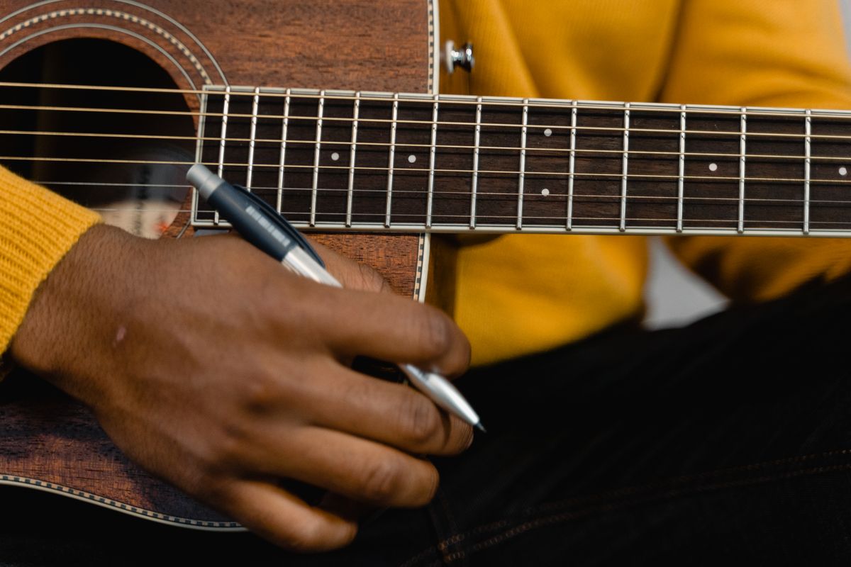Taylor Swift Songs Disappear From Trump and White House Social Media Posts 3 A detailed view of a hand holding a pen on an acoustic guitar, highlighting musical creativity.