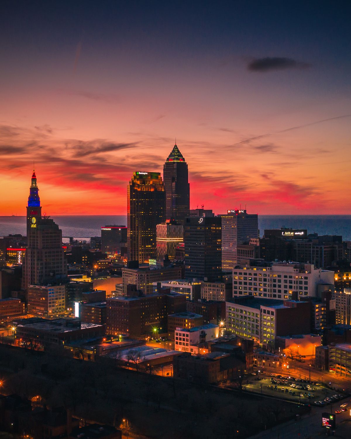A vibrant cityscape during sunset with illuminated skyscrapers and a colorful sky.