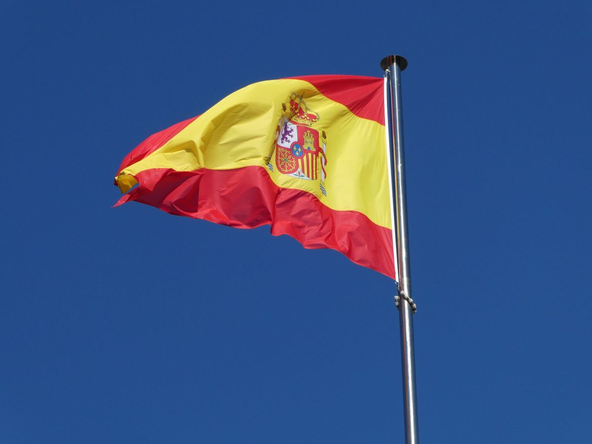 A vibrant Spanish flag prominently waving against a clear blue sky, symbolizing national pride.