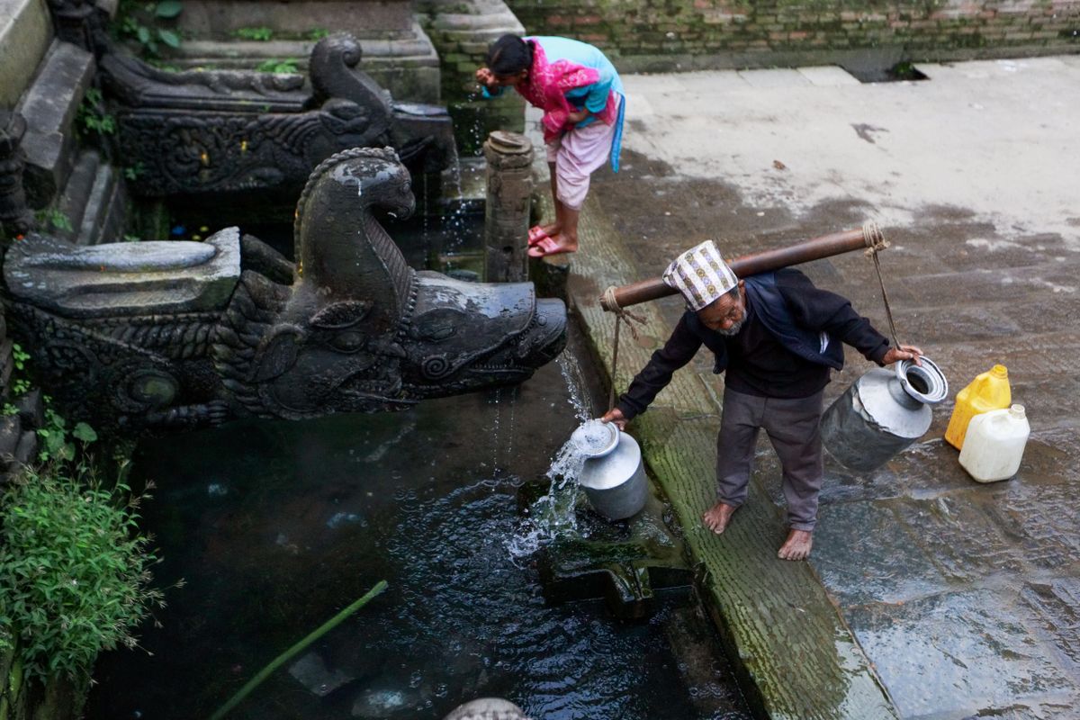 An elderly man collects water from a traditional stone tap in a cultural setting, reflecting daily life.