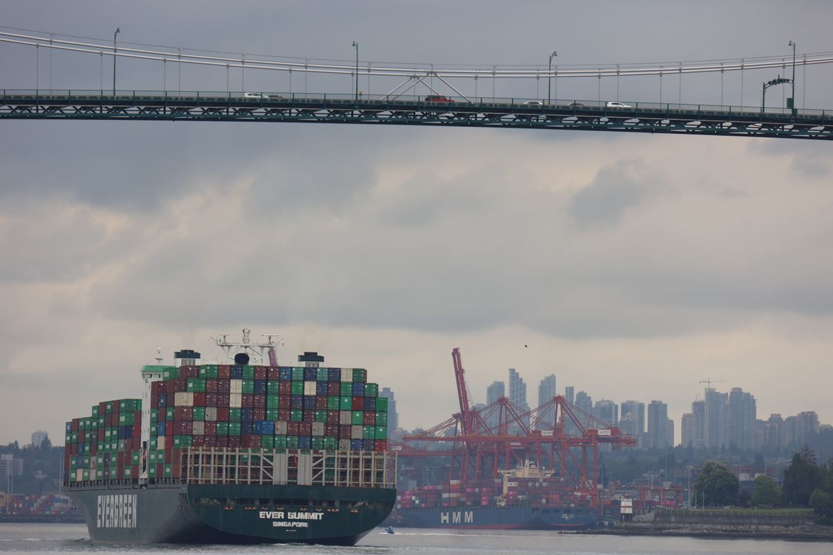 Container ship traverses under Lions Gate Bridge with Vancouver skyline backdrop, showcasing logistics and transport.