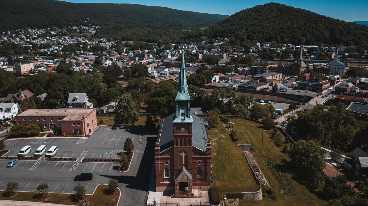 Drone view of aged temple facade near parking with vehicles behind residential houses in mounts