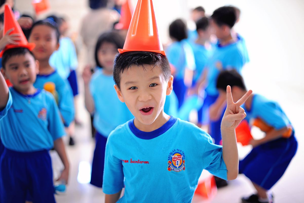 Joyful children in blue uniforms having fun and posing with traffic cones indoors.