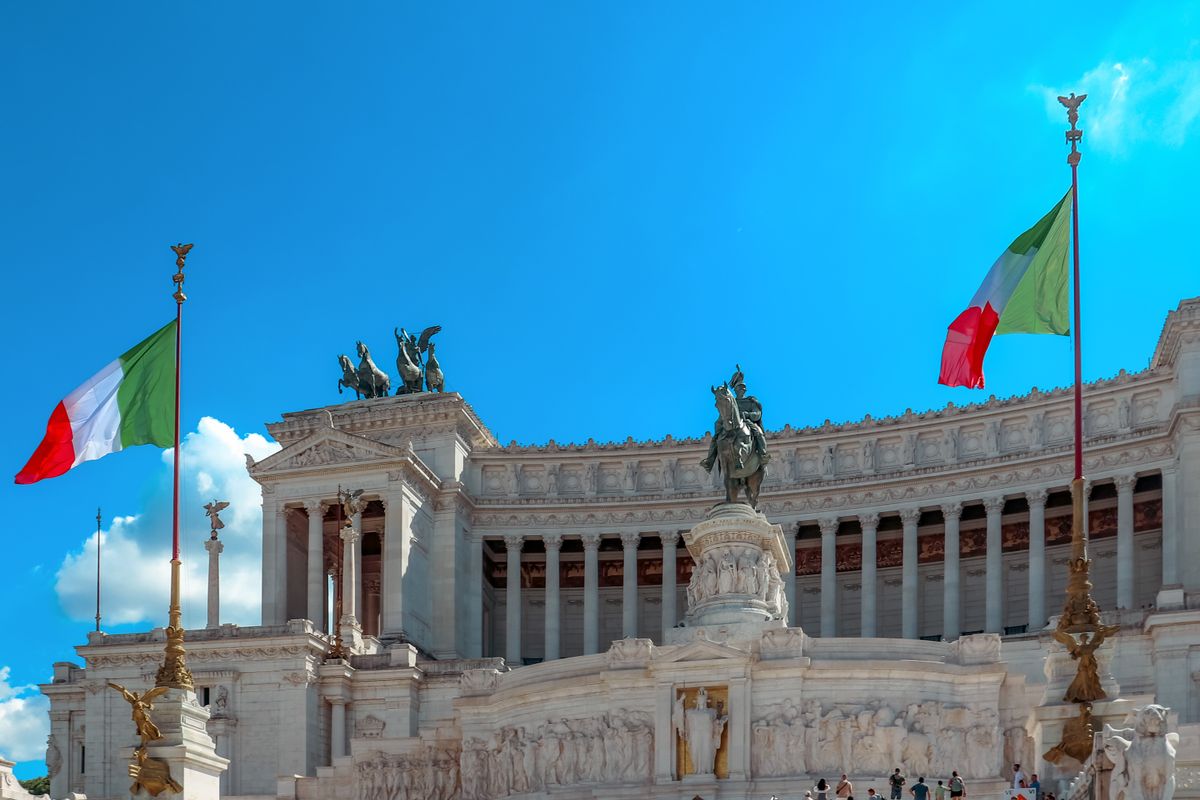 Majestic view of the Altare della Patria in Rome with Italian flags fluttering under a clear blue sky.