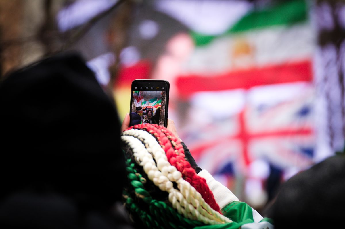 Minnesota Water Cyberattacks Expose a Frightening American Weakness as Trump and Walz Trade Blame 2 Person using smartphone to capture live event in Brussels with visible flags in background.