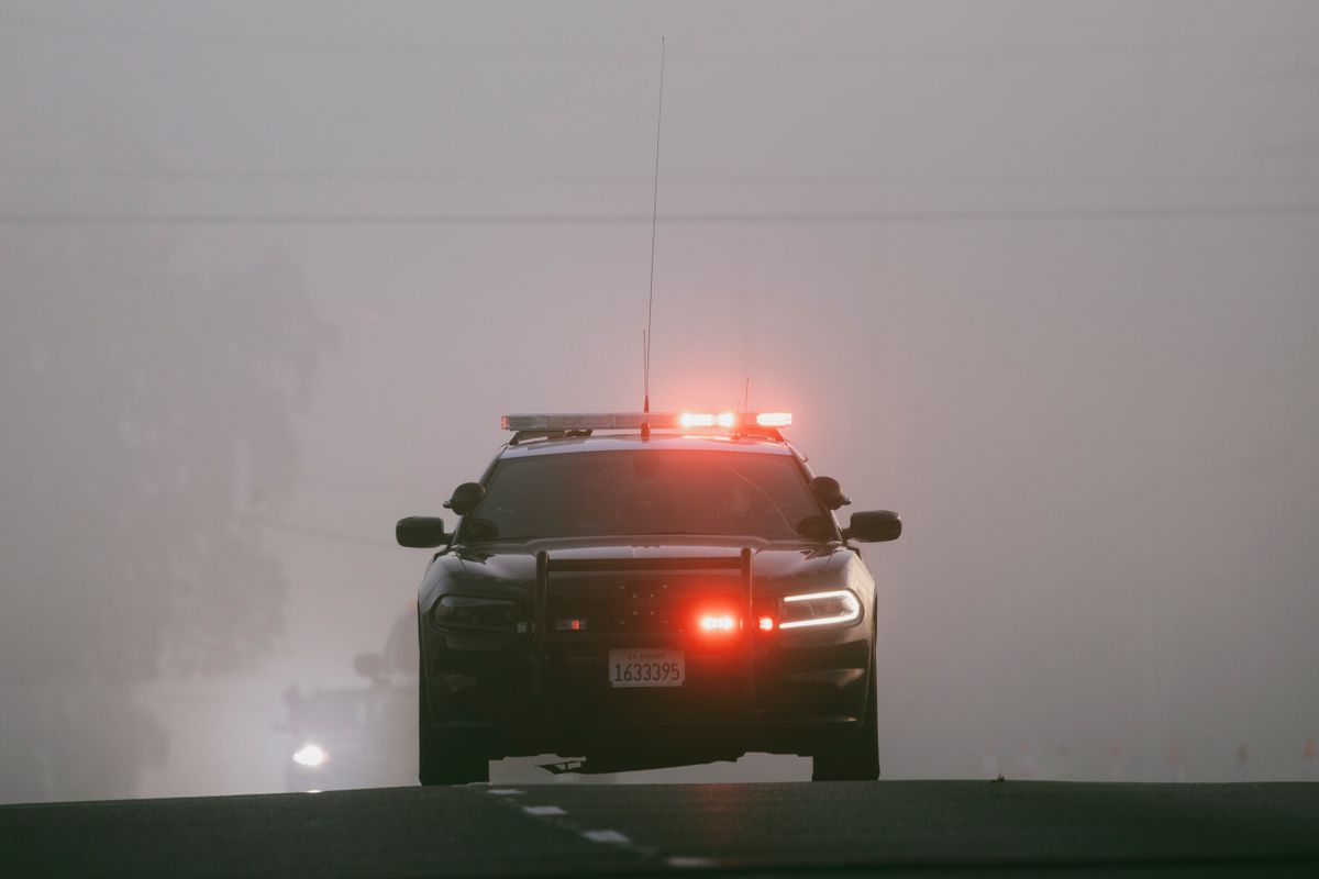 Unlicensed Driver Arrested After Fatal Parker County Crash That Killed Two Women 1 Red lights illuminate a foggy road as a police car approaches, creating an intense atmosphere.