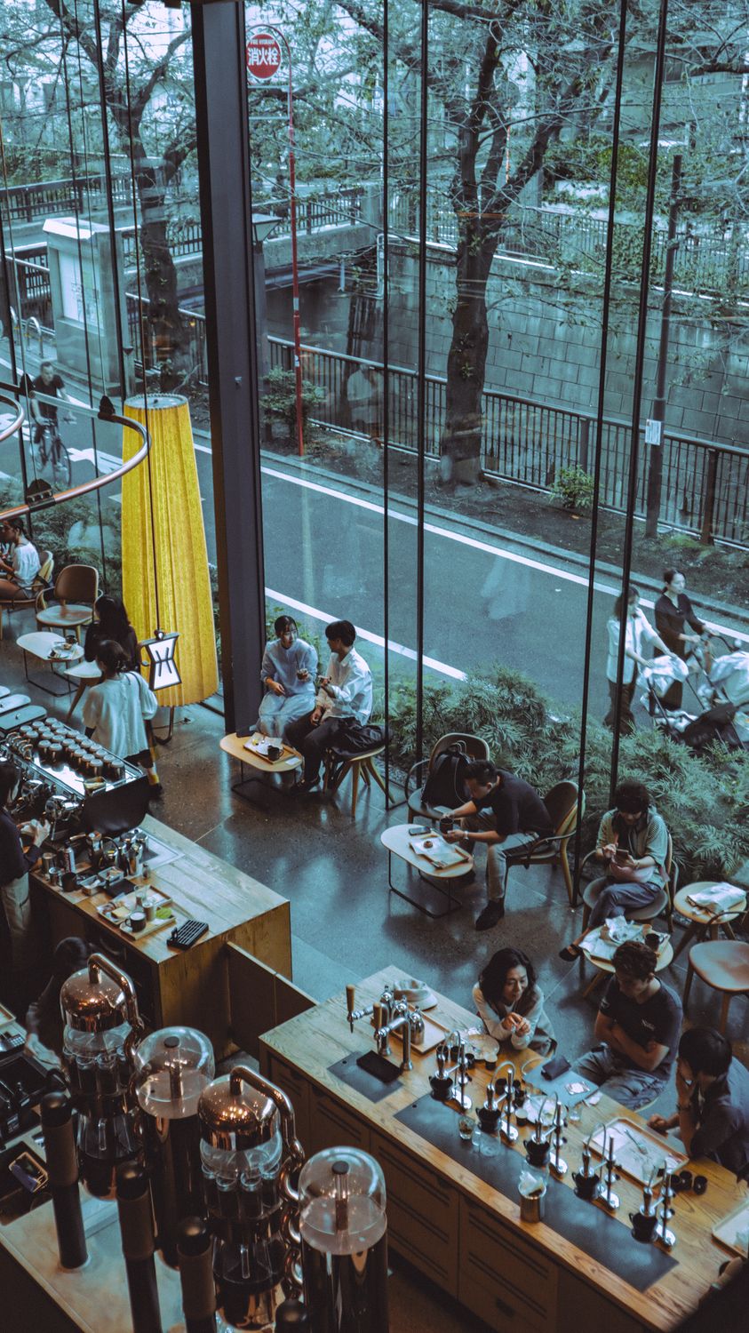 From Farmers’ Market Favorite to Houston Café: The Couple Turning Family Recipes Into a Neighborhood Destination 2 Urban cafe scene in Tokyo with people dining against a large glass window view of the street.