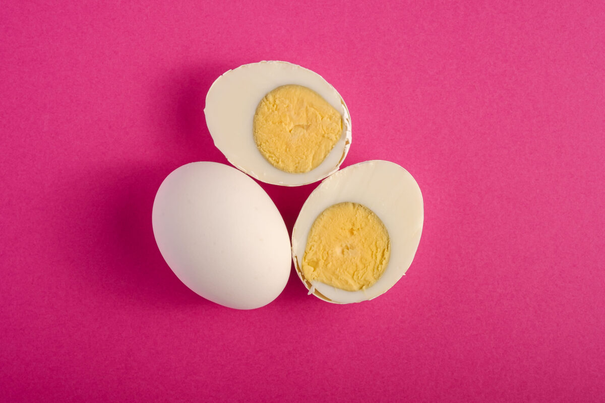 Boiled egg with yellow yolk near to white eggs on vibrant purple pink plain minimal background, top view, happy Easter day