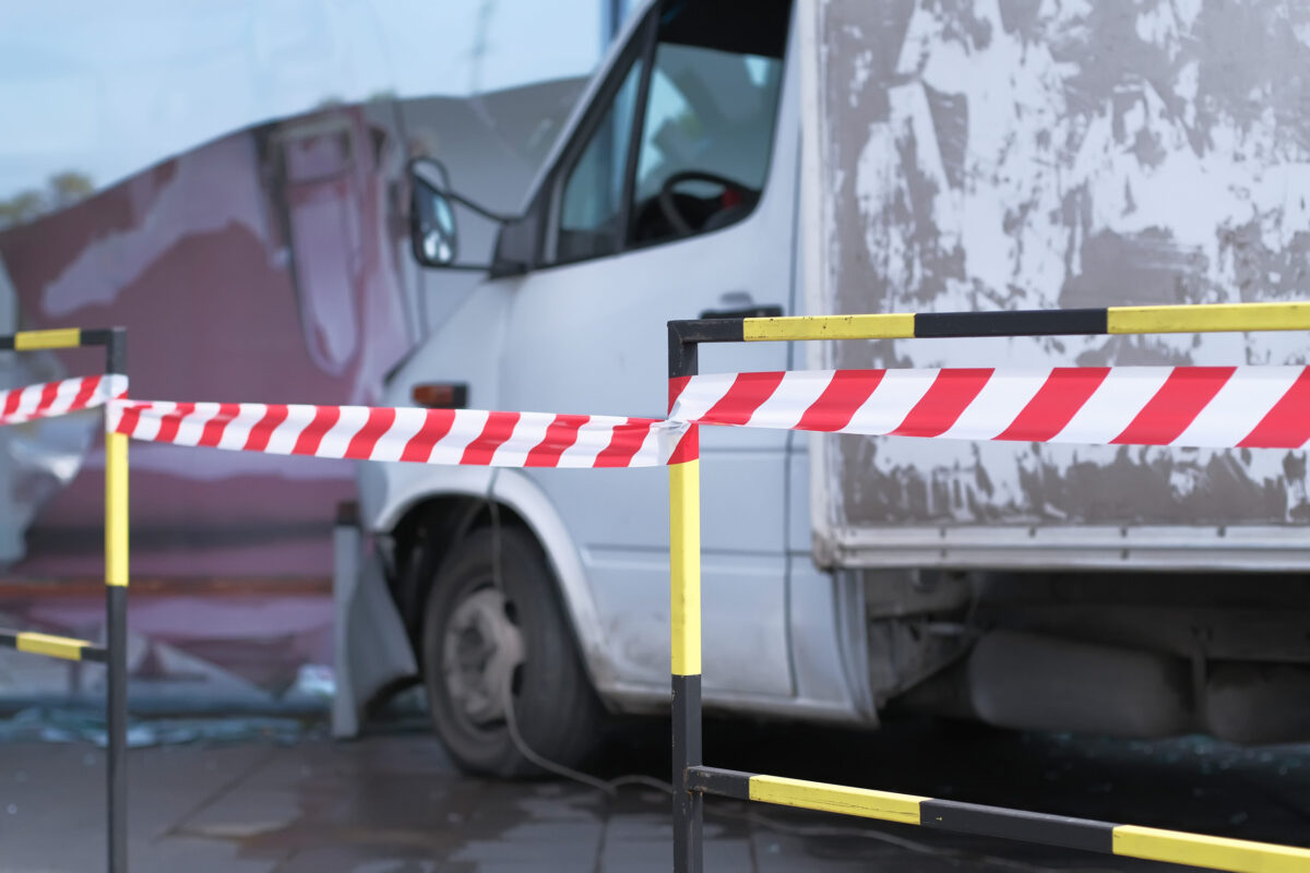 White lorry collided with a glass wall of shopping mall. Road accident site is isolated and fenced off with a signal tape.