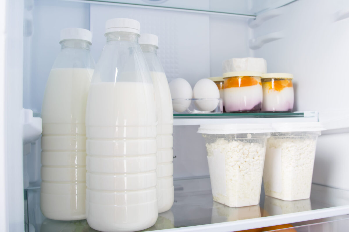 against the background of a white refrigerator, there are products, milk, eggs, cottage cheese and yogurt on glass shelves