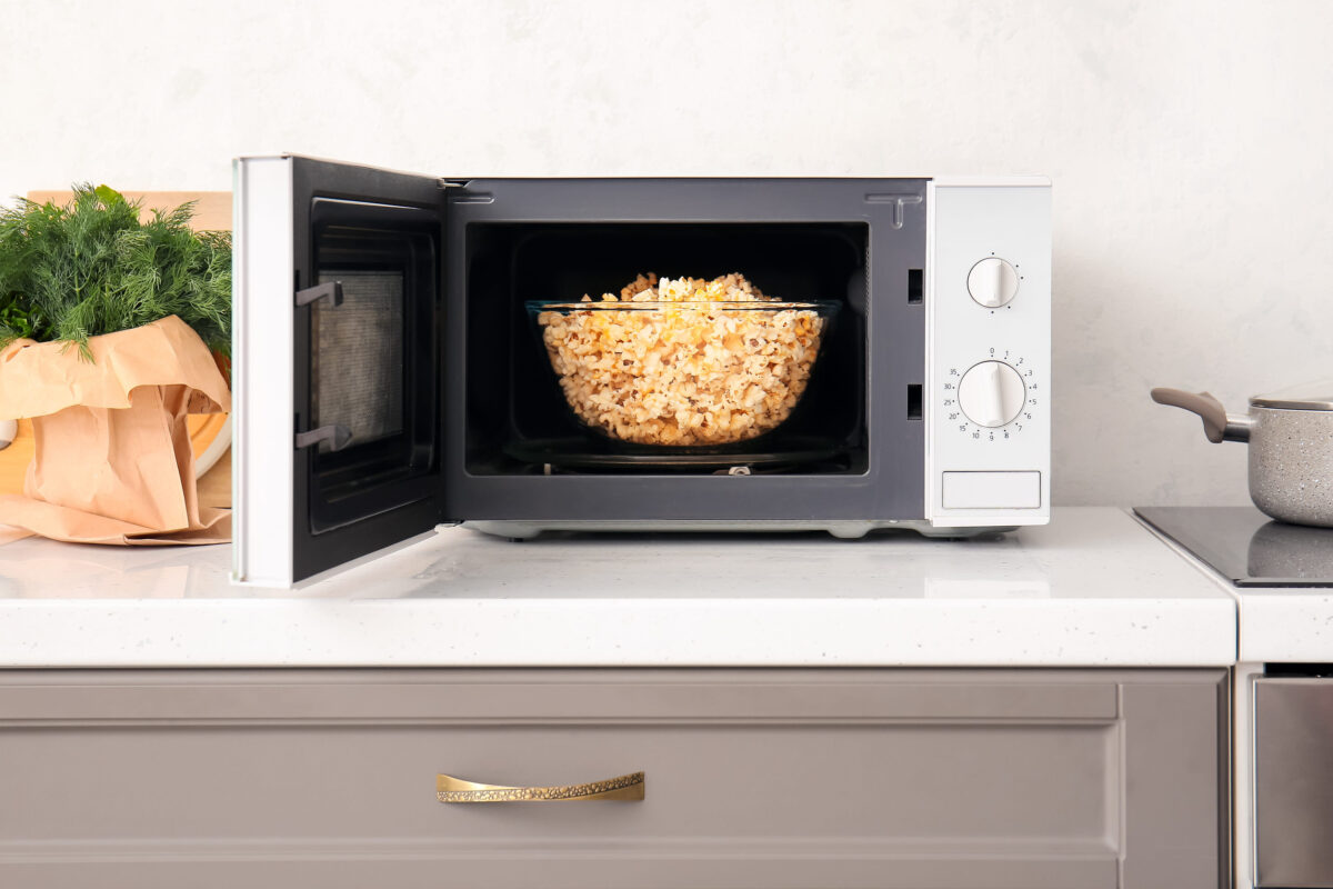 Modern microwave oven with bowl of popcorn on counter near light wall