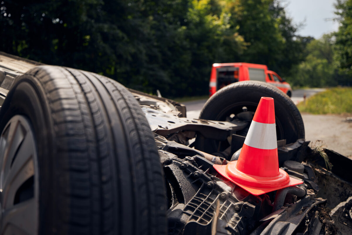 Damaged car on the roof after accident against fire rescue vehicle. Selective focus on traffic cone.