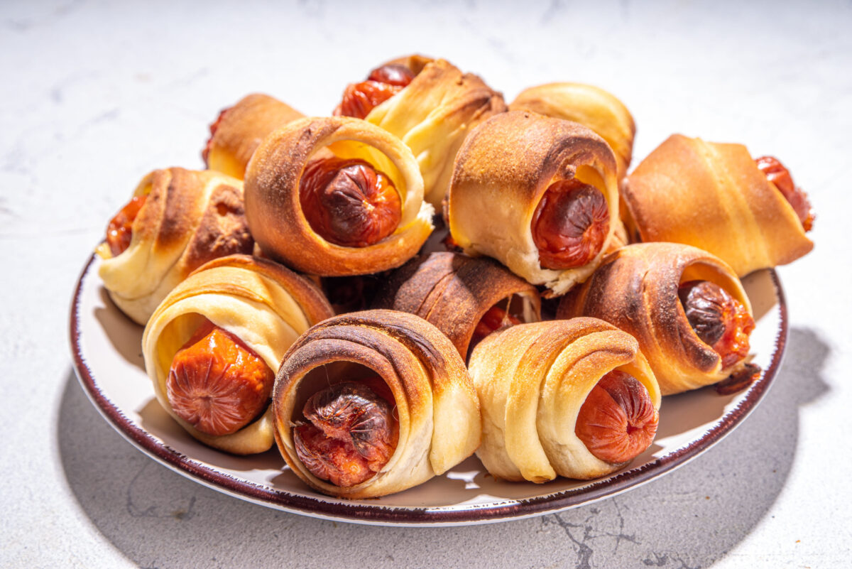 Oktoberfest party food. Pretzel hot dogs, puff pastry rolls with sausage and bacon, traditional Bavarian German Pigs in blanket on Oktoberfest decorated table background
